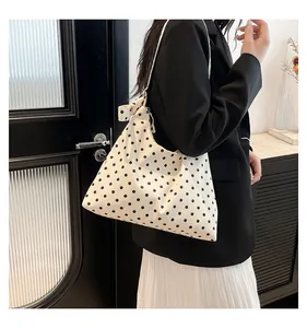 Dettaglio della borsa tote in tela a pois neri con un fiocco decorativo sulla tracolla