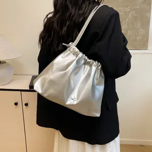 Silver metallic pleated drawstring tote bag with bow detail worn over the shoulder