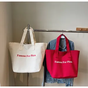 Detail von roten und cremefarbenen Canvas-Tragetaschen mit Famous For Pizza-Aufdruck an Haken