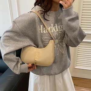 Sac hobo beige chic avec logo doré et pompon porté par un mannequin élégant en intérieur