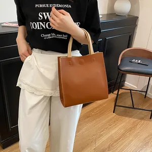 Vertical brown tote bag with white handles and round embossed detail for women