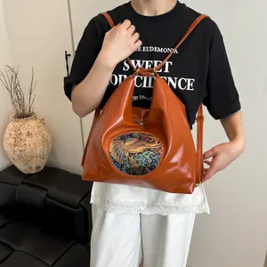 Versatile orange leather shoulder bag with elephant embroidery in a stylish room setting