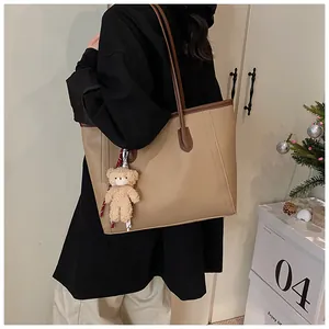 Detailed side view of large khaki leather tote bag with brown straps and plush bear charm