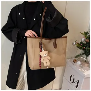 Detail of khaki tote bag with litchi texture leather and a cute plush bear charm