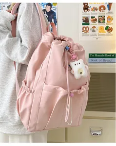 Detalle de mochila rosa con cordón, bolsillos laterales y un peluche de oso colgante
