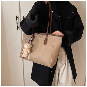 Detail view of khaki pebbled leather tote bag with a cute teddy bear charm on shoulder