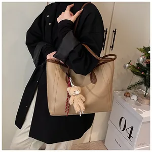 Close-up of khaki tote bag with dark brown leather straps and cute teddy bear pendant