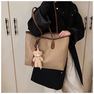 Detail of khaki tote bag with litchi texture, brown trim, and a cute teddy bear charm