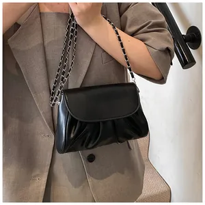 Detail view of a black pleated crossbody bag with a metallic chain strap on a model