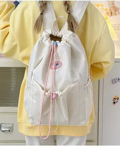 Detalle de una mochila blanco crema con cordón, insignia de dibujos y bolsillos laterales