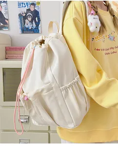 Detalle de mochila blanca con cordón, bolsillos laterales y colgante de peluche en cuarto