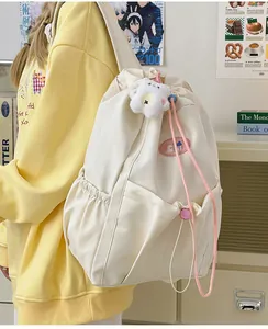Detalle de la mochila de lona crema con cordón, bolsillo lateral y colgante de osito de peluche