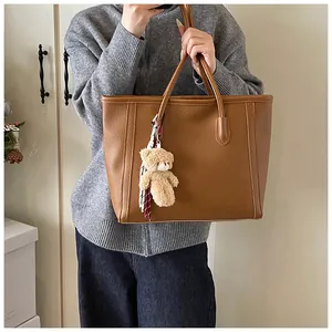 Brown litchi grain tote bag with bear charm and striped scarf detail for daily commuting