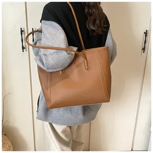 Detail of large brown lychee grain leather tote bag worn by a model in a minimalist setting