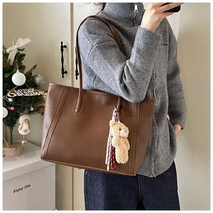Detail of a large brown lychee leather tote bag with a plush bear and silk scarf charm