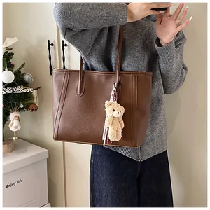 Detail of brown litchi pattern leather tote bag with plush bear and silk scarf charm
