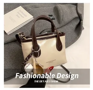 Detail of cream bucket bag with brown contrast trim and baseball charm on a grey coat