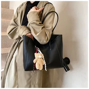 Macro detail of the black pebbled leather texture on a spacious tote bag with a bear charm