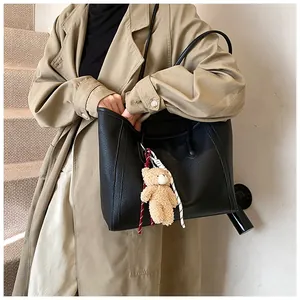 Macro detail of black lychee grain tote bag with plush bear charm on camel trench coat