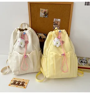 Detalle de mochilas de nailon con cordón en crema y amarillo con colgante de osito