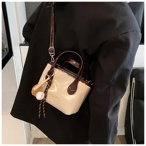 Dettaglio di una borsa a secchiello minimalista con finiture a contrasto e ciondolo