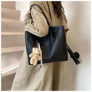 Detail of black tote bag in lychee leather texture with a cute plush bear pendant