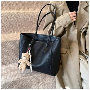 Detail of black pebbled leather tote bag with cute bear charm on warm carpeted stairs