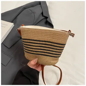 Primer plano del bolso saco de paja tejida con rayas negras y correa de cuero marrón