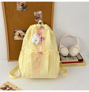 Detalle de mochila amarilla con cordón, colgante de oso y múltiples bolsillos