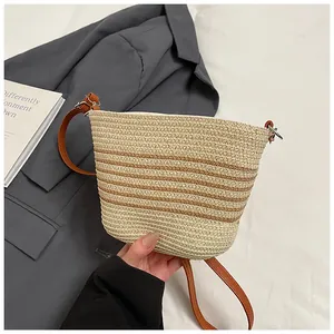 Detalle de bolso de paja a rayas con correa de cuero marrón y anilla de metal