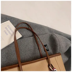 Detail of khaki lychee grain leather tote bag with brown handles and small ball charm