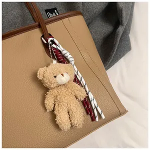 Close-up of curly plush bear keychain and braided tassels on a pebbled leather tote bag