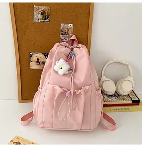 Detalle de la mochila de nailon rosa con cordón, colgante floral y bolsillo frontal