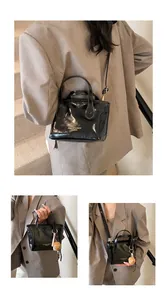 Dettaglio della borsa a secchiello nera lucida con scritta fashion e ciondolo a orsetto