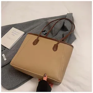 Macro shot of minimalist lychee grain leather tote bag with dark brown handles on a wool coat