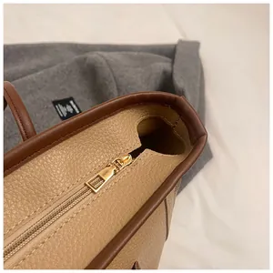 Macro detail of lychee grain leather tote bag featuring gold zipper and contrast stitching