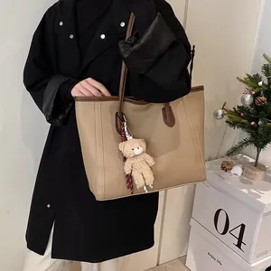 Large khaki tote bag with brown handles and teddy bear charm shown in studio setting