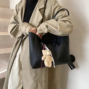 Large black pebbled leather tote bag with bear keychain on a woman in a beige trench coat