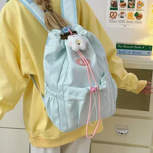 Mochila minimalista azul claro con cordón, colgante de oso y bolsillos laterales