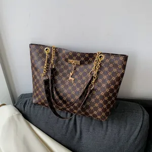 Brown tote bag with golden geometric floral print, metal chain straps, and deer charm