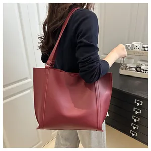 Detail shot of a large burgundy matte leather tote bag worn as a shoulder bag