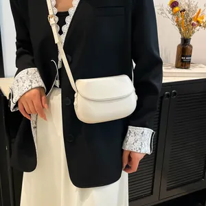 Close-up of a white leather saddle bag on a model wearing a black blazer and white skirt