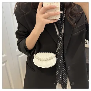 Detail of a white shell-shaped crossbody bag with pearl accents and a gold chain strap