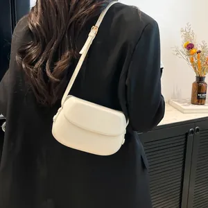 Close-up of a beige faux leather saddle bag with gold hardware worn over a black blazer