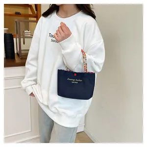 Detail of navy canvas tote bag featuring woven rope handles and red button closure