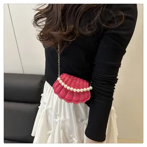 Close-up of shell-shaped rose pink crossbody bag with pearl handle and golden chain