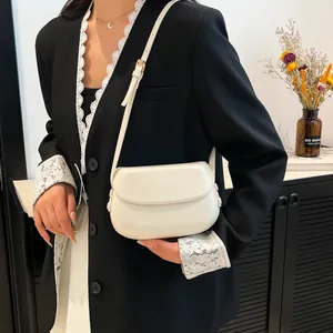 Model wearing a minimalist cream-colored saddle bag with adjustable gold hardware strap