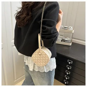 Détail du sac cylindrique crème avec chaîne dorée et motif de lettres sur un mannequin