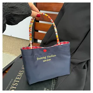 Dettaglio dei manici intrecciati colorati e bottone rosso sulla borsa tote in tela blu