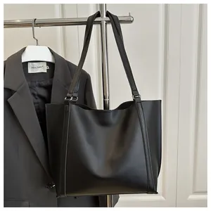 Close-up of matte black leather tote bag showing reinforced side stitching and long straps